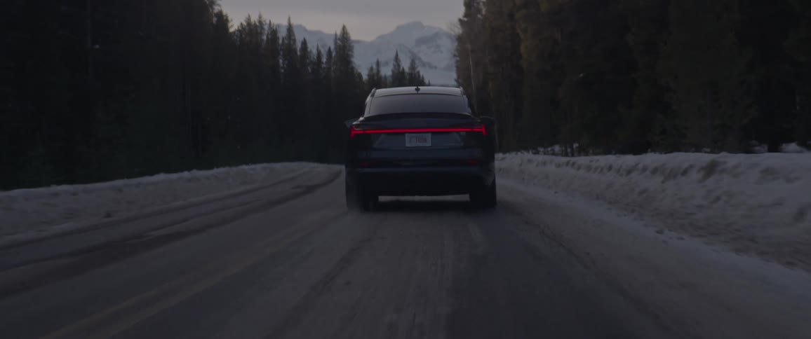 A vehicle driving on a snowy road with trees a mountain range the sky and clouds in the background