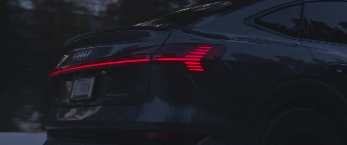 An audi vehicle drives on a rural road beside lots of trees