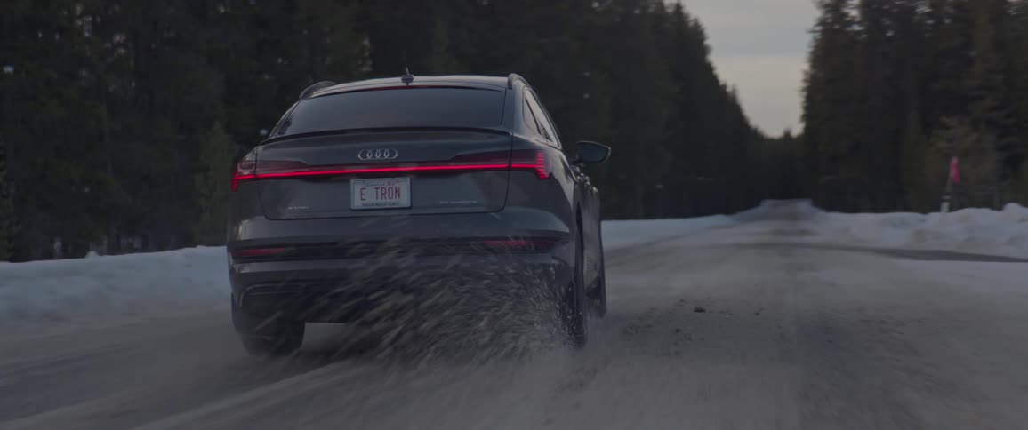 Audi car drives on snowy forest road at dusk