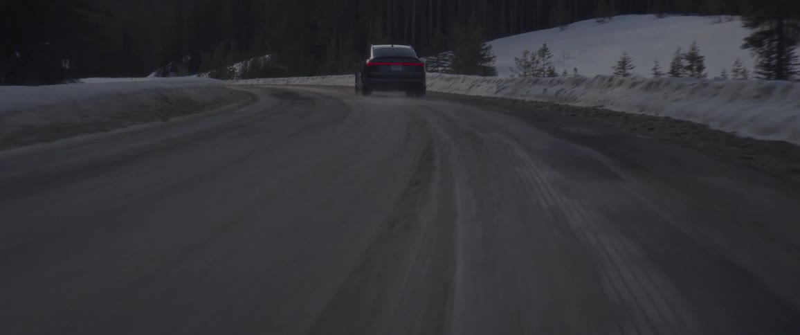 A vehicle driving on a snowy road with signs and trees in the background