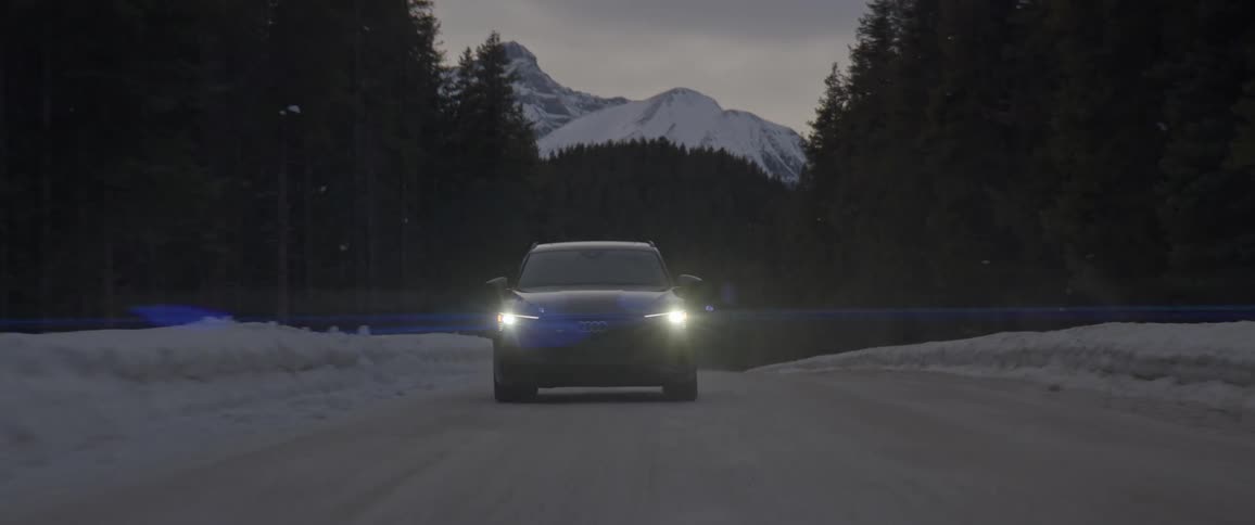 Black sports car with headlights on driving on a rural road through the forest near the mountains