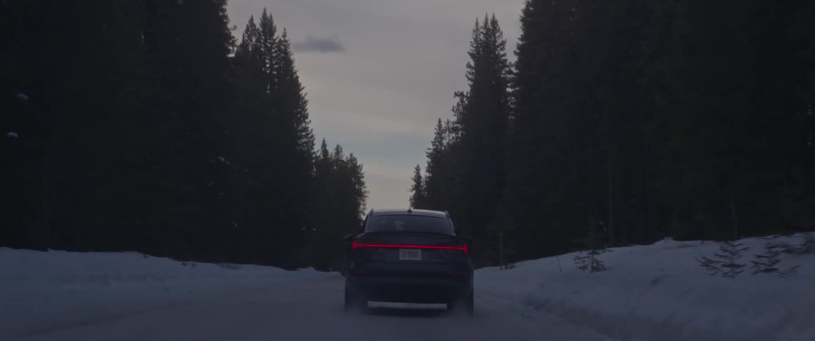 A car travels on a snow covered forest road surrounded by tall trees
