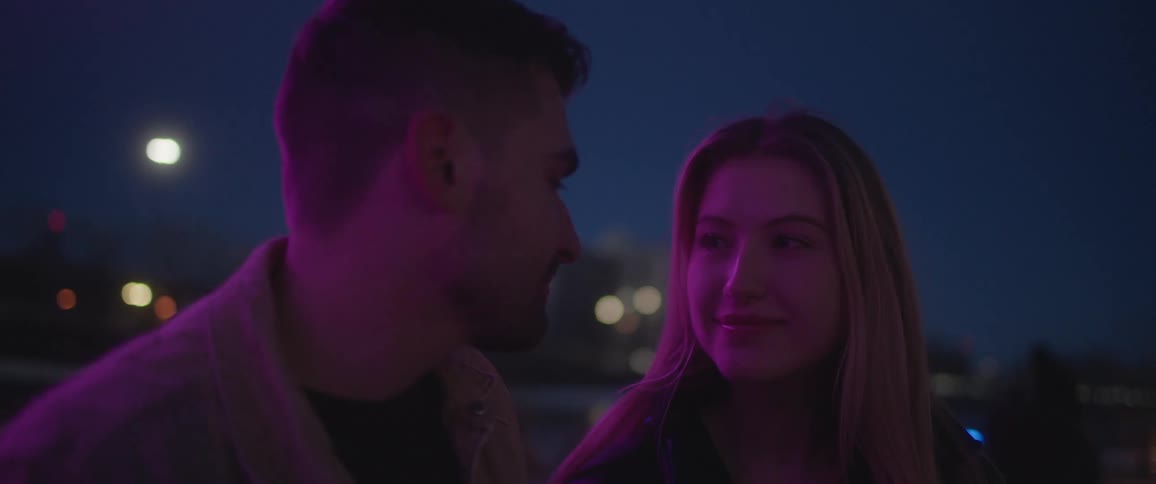 A man leans in to kiss his date as they hang out on a downtown rooftop