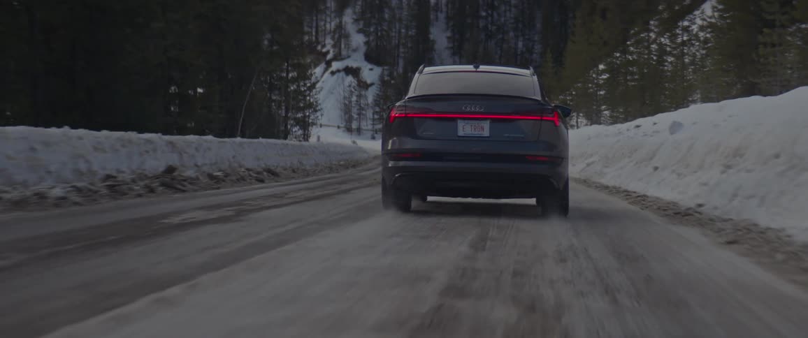 A black car travels on a road with snow and trees all around