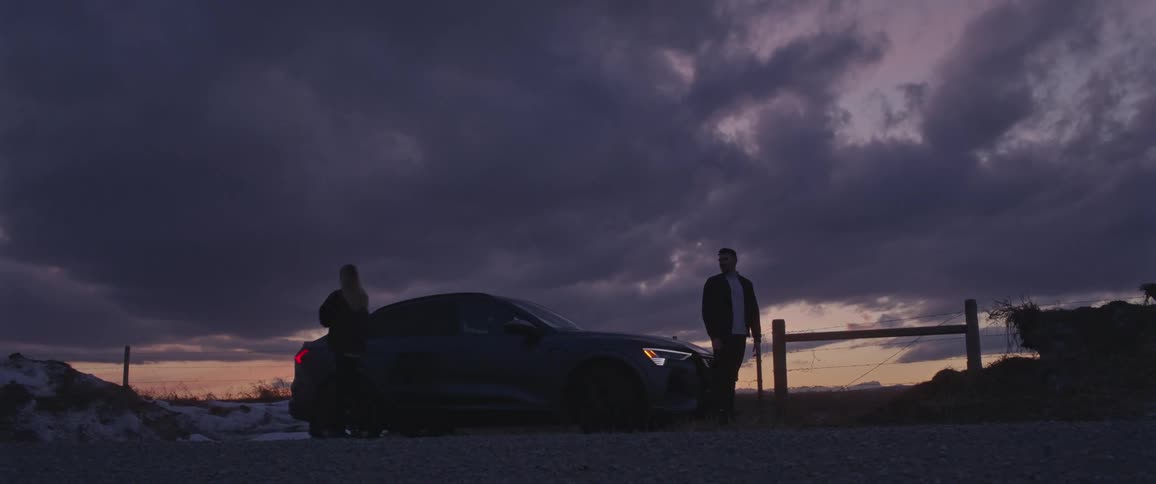 A man and woman argue and the woman walks away from the man and behind the car where they are standing