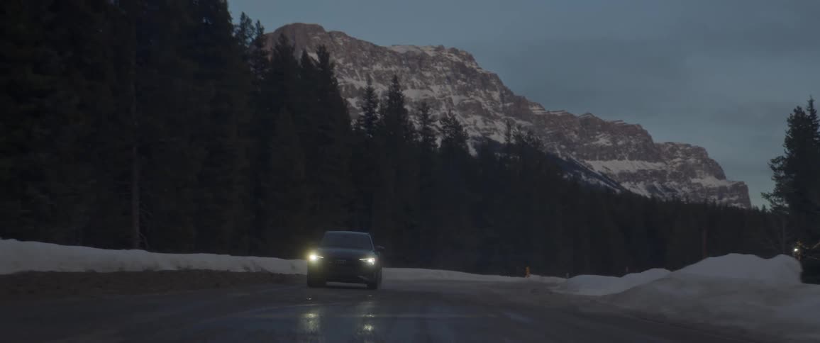 A black car is driving on a road during snowy season