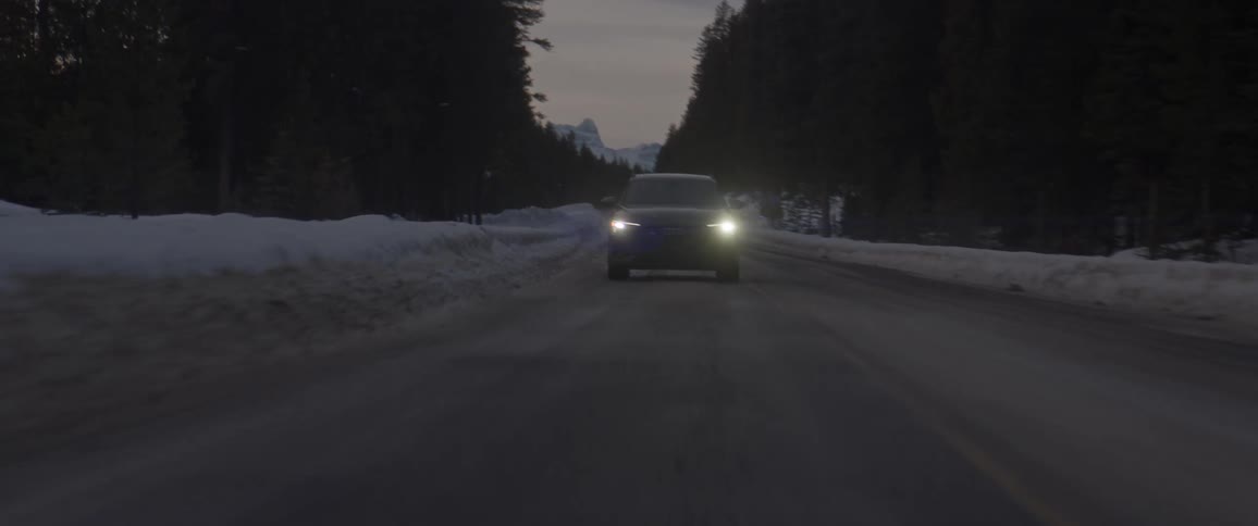 Dark grey audi car drives on snowy forest road at dusk