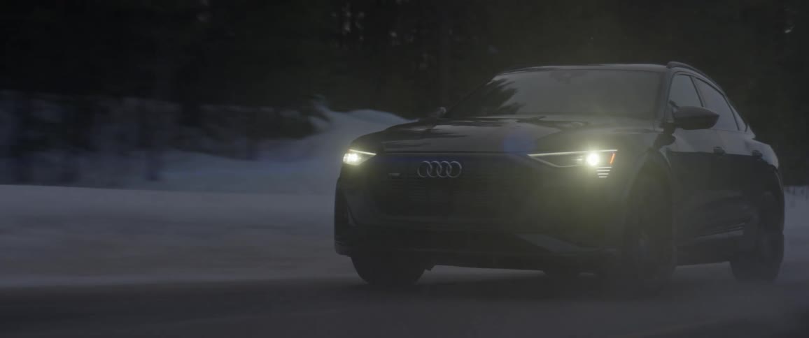 A vehicle driving on a snowy road with trees the sky and clouds in the background