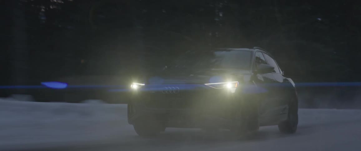 A single automobile speeds along a road that is lined with snow and trees