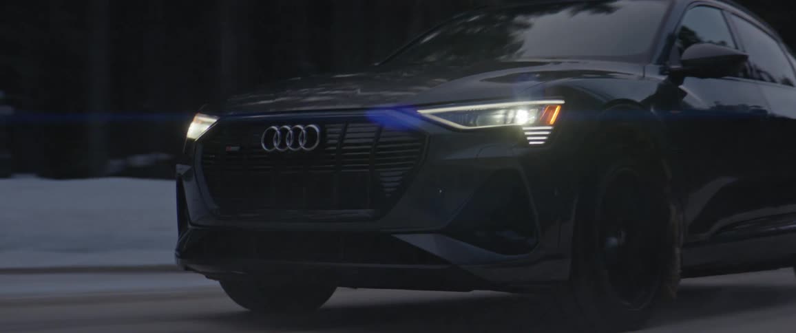 A black audi car is driving on a road during snowy season