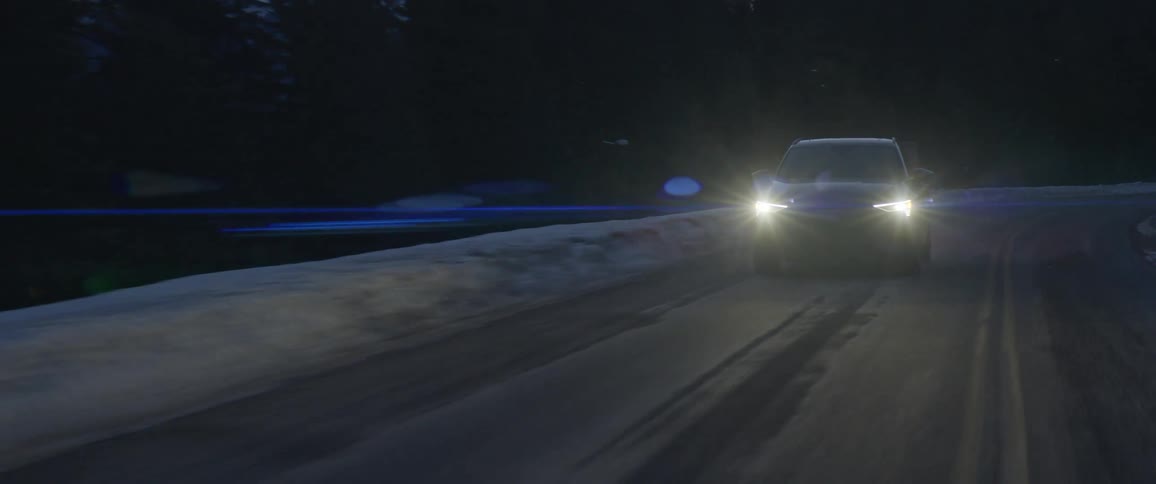 A vehicle driving on a snowy road with trees the sky and clouds in the background