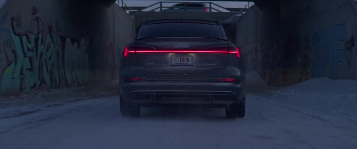 A black car travels under a bridge on a snow covered road