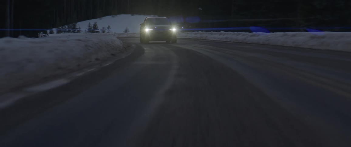 A car drives down a road with a snow covered bank