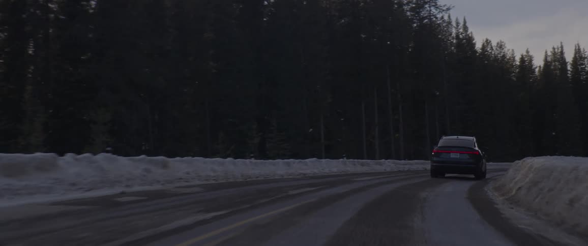 A vehicle driving on a road with trees the sky and clouds in the background