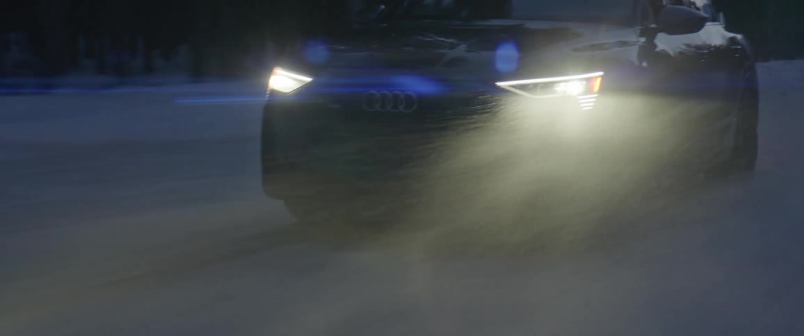 A black audi car travels on a snow covered road with headlights on