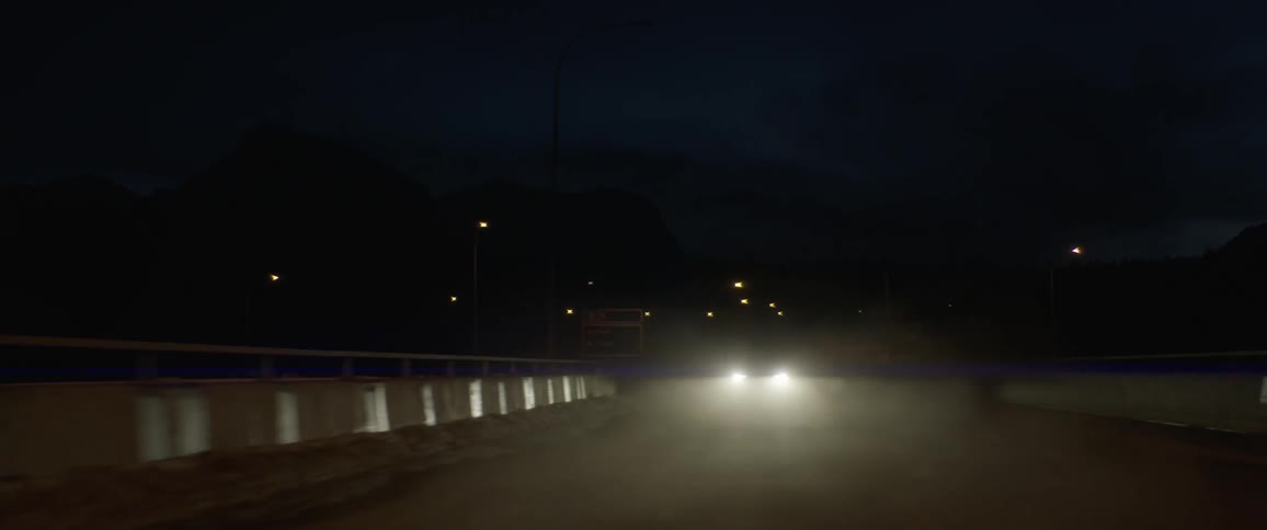 A vehicle with headlights driving on a snowy road with the sky and clouds in the background