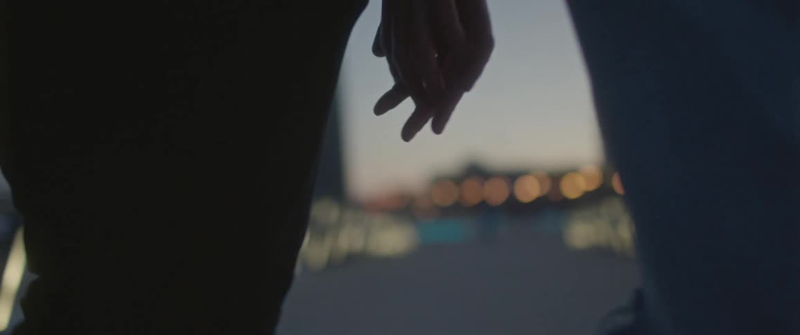 A man and a woman walking and holding hands with the sky and clouds in the background