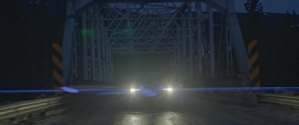 Black sports car driving over a bridge in the countryside near the mountains at night