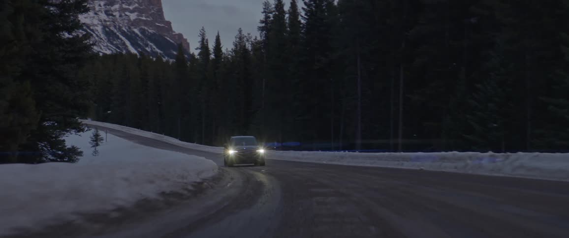 A vehicle driving on a road with a mountain range the sky and clouds in the background