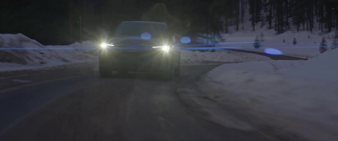 A vehicle travels along a road through a snowy forest in the evening