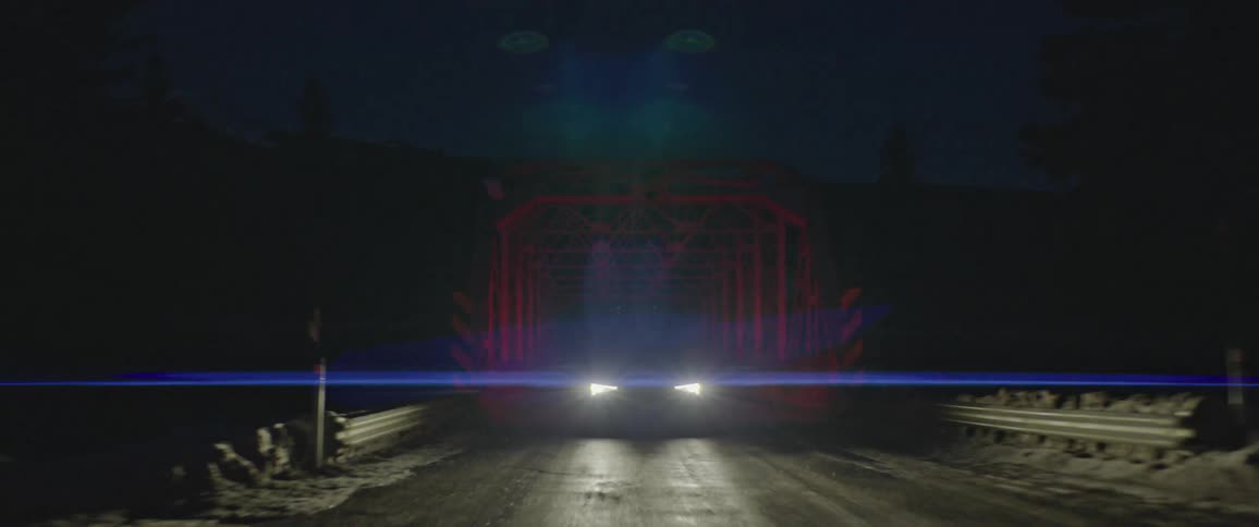 Black sports car driving over a bridge in the countryside near the mountains at night