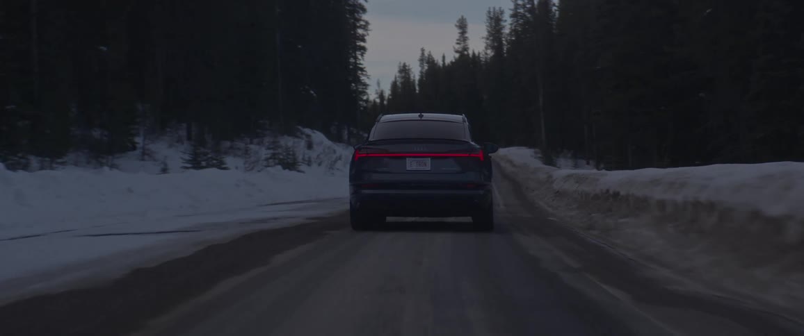 A car drives on a road next to a snowy forest