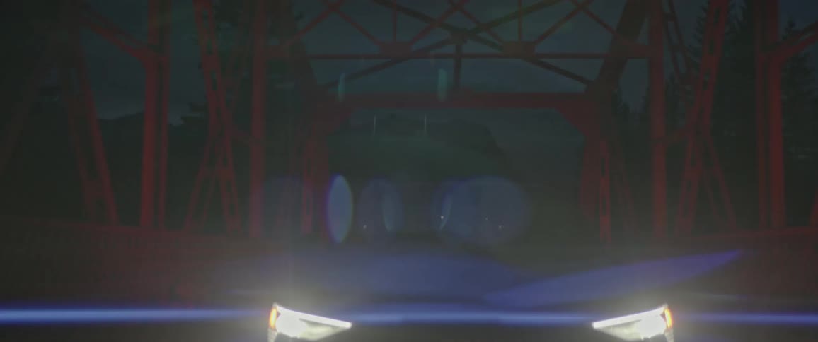 Car headlights light up road as vehicle crosses red metal bridge at night