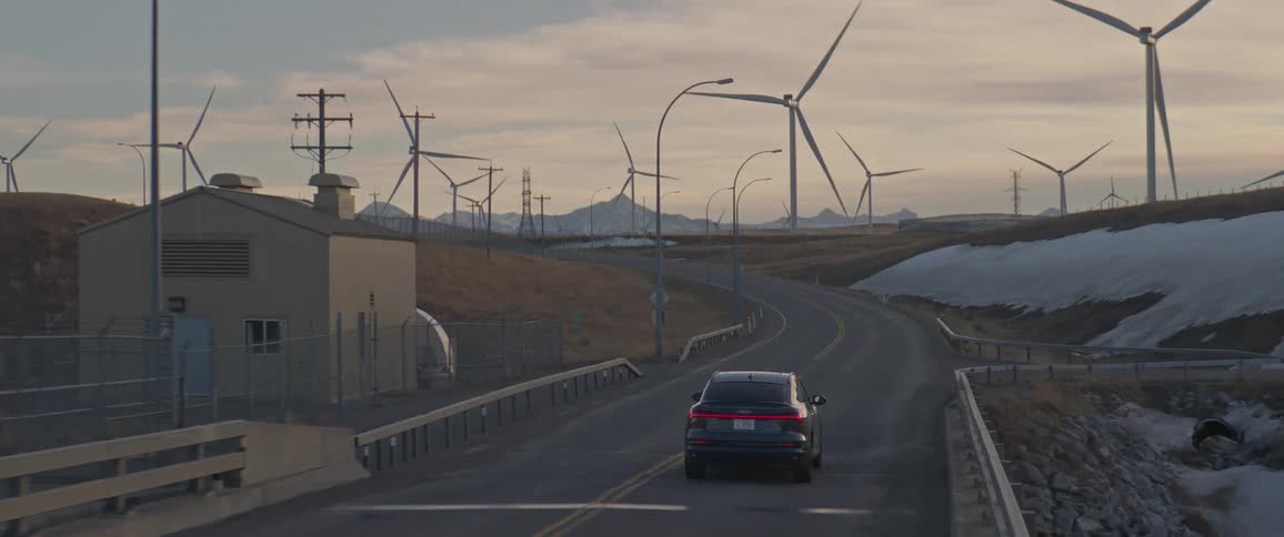 A black car travels on a road through a wind farm of spinning turbines