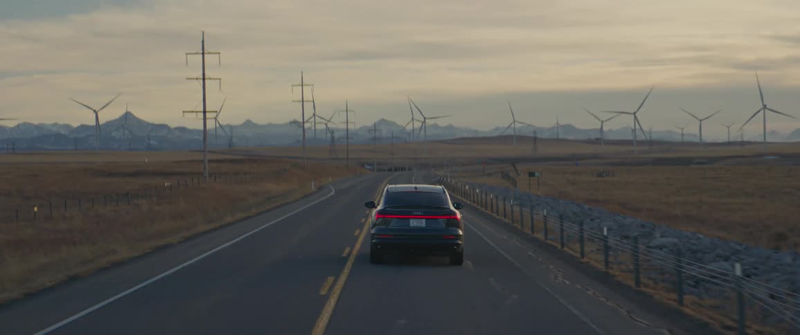 A vehicle driving on a road with wind turbines the sky and clouds in the background