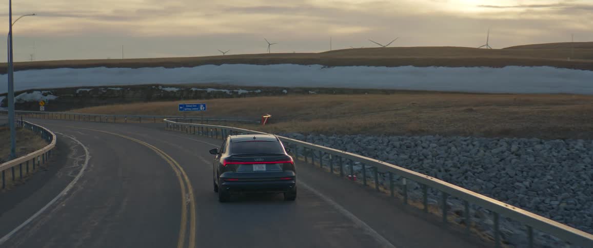 A vehicle driving on a road with wind turbines the sky and clouds in the background