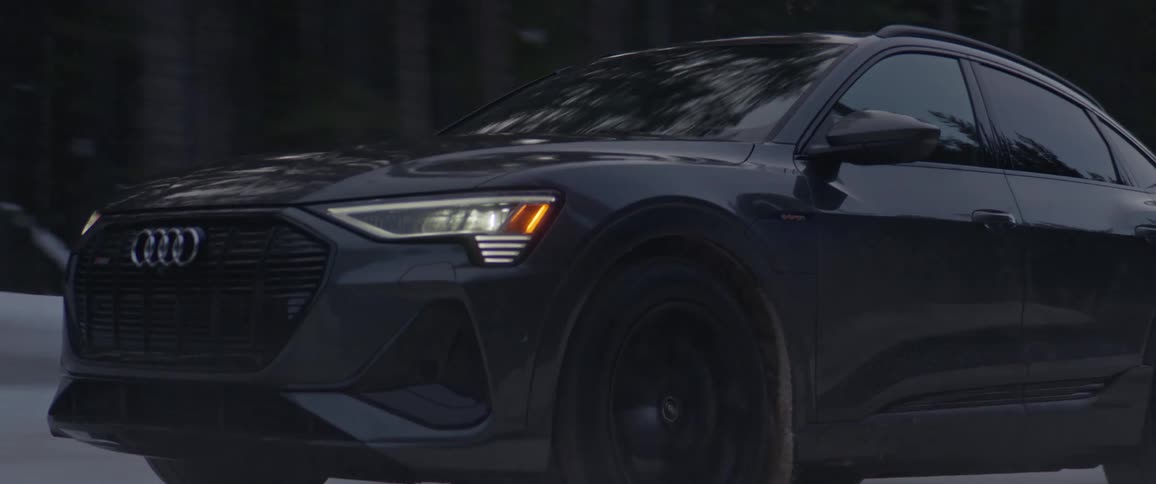 Dark grey audi car drives on snowy forest dirt road
