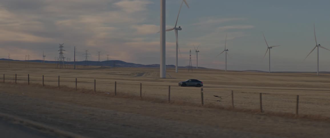 Audi car drives in wind farm next to wind turbines