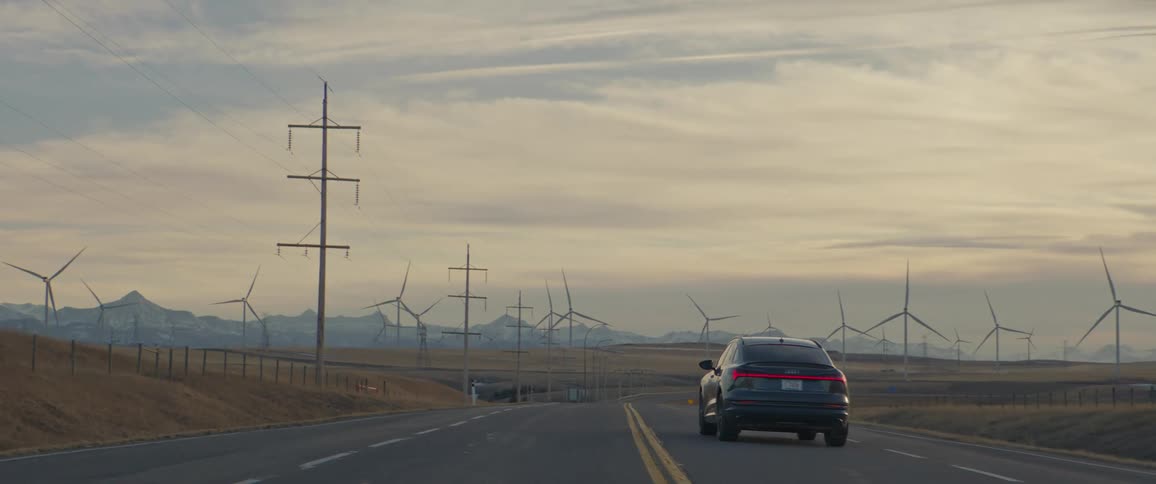 Car driving on a road near a wind farm at evening