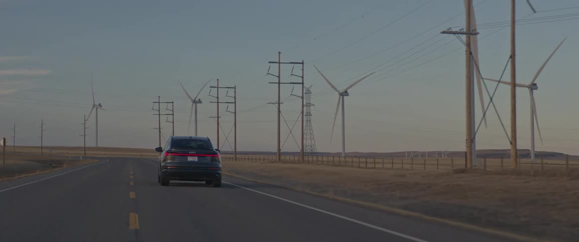 A vehicle driving on a road with wind turbines the sky and clouds in the background
