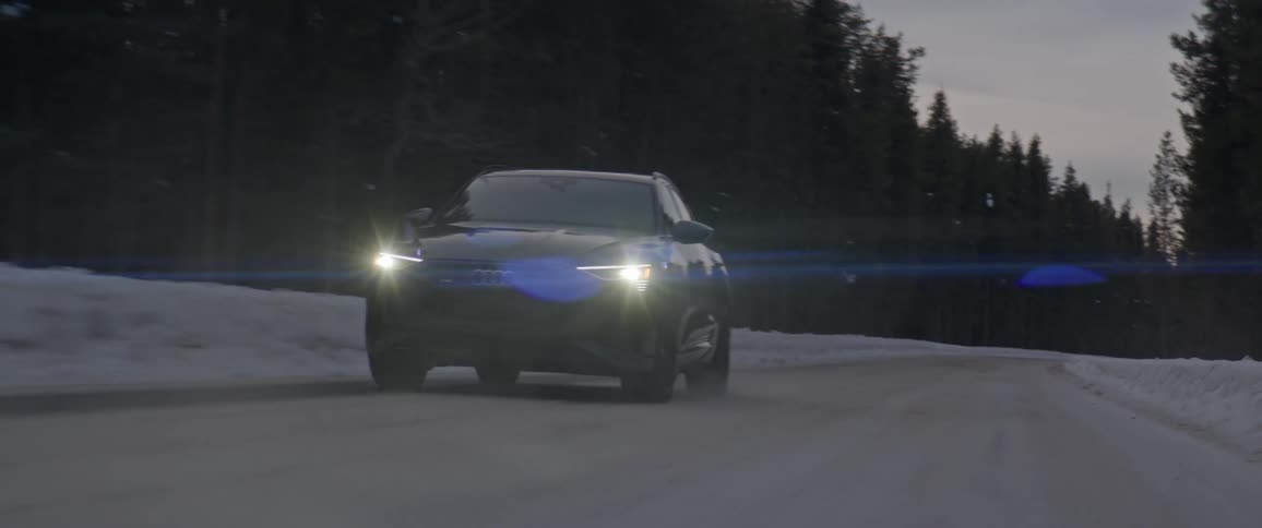 Black car driving on a snow covered road in the countryside through the pine tree forest at morning