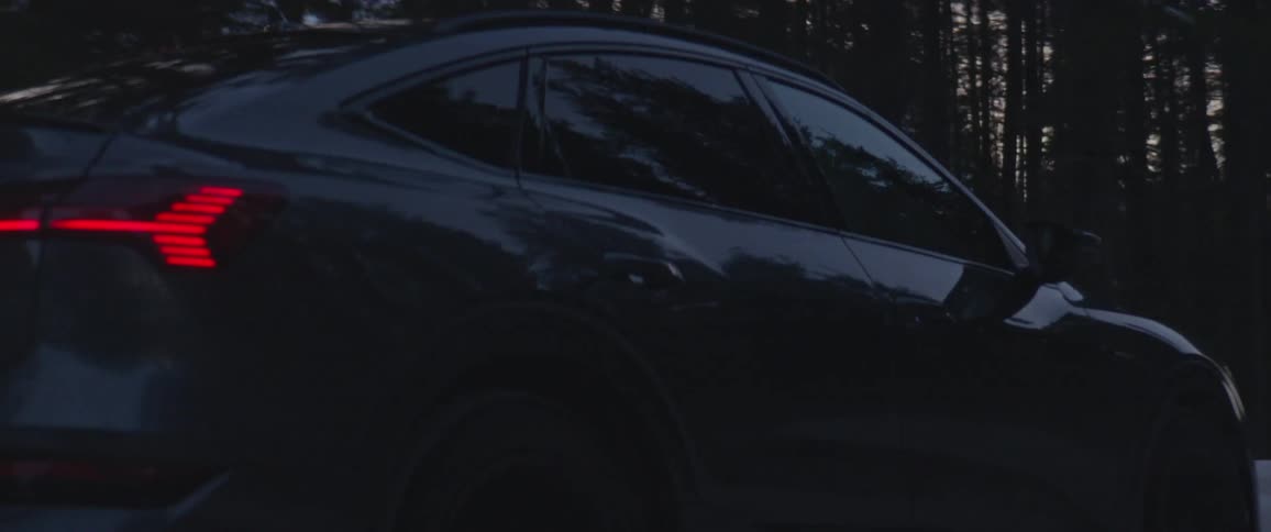 Audi car drives on snowy forest road at dusk
