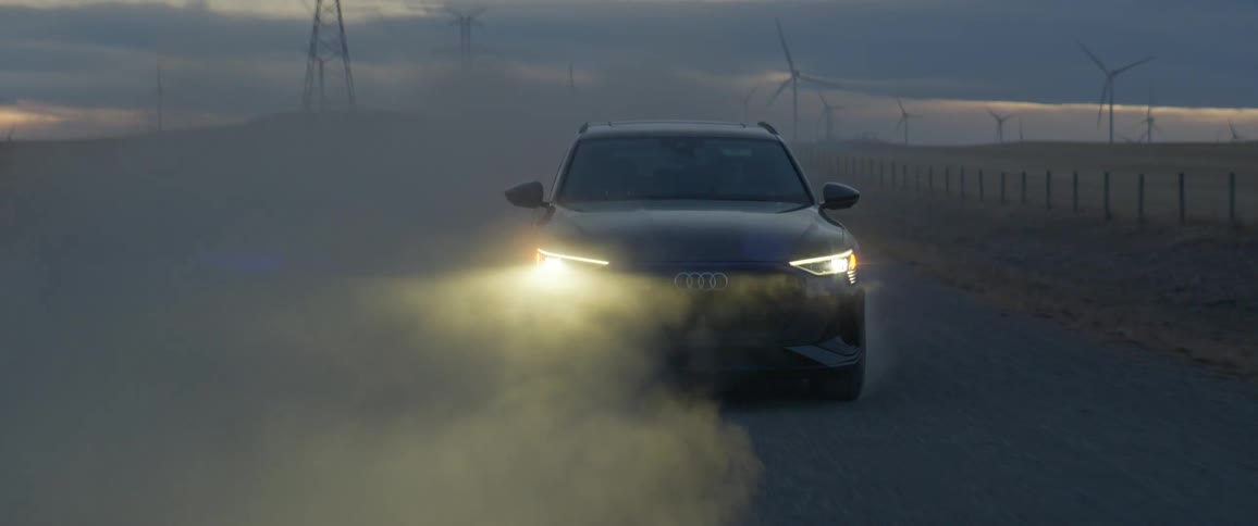 A vehicle driving on a road with wind turbines the sky and clouds in the background