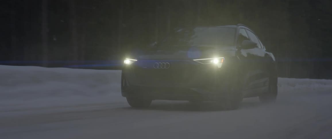 Audi car drives on snowy forest road at dusk