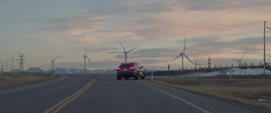 Audi car drives on highway next to wind farm at dusk