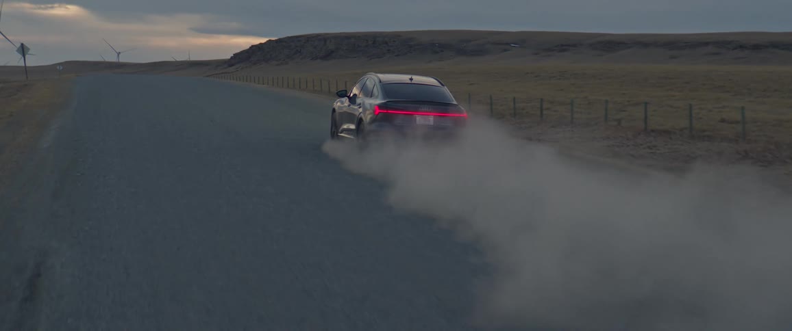 A black car travels on a road with spinning wind turbines along the roadside