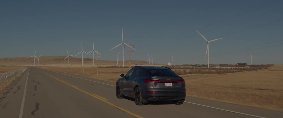 A vehicle drives on a road beside a wind turbine field