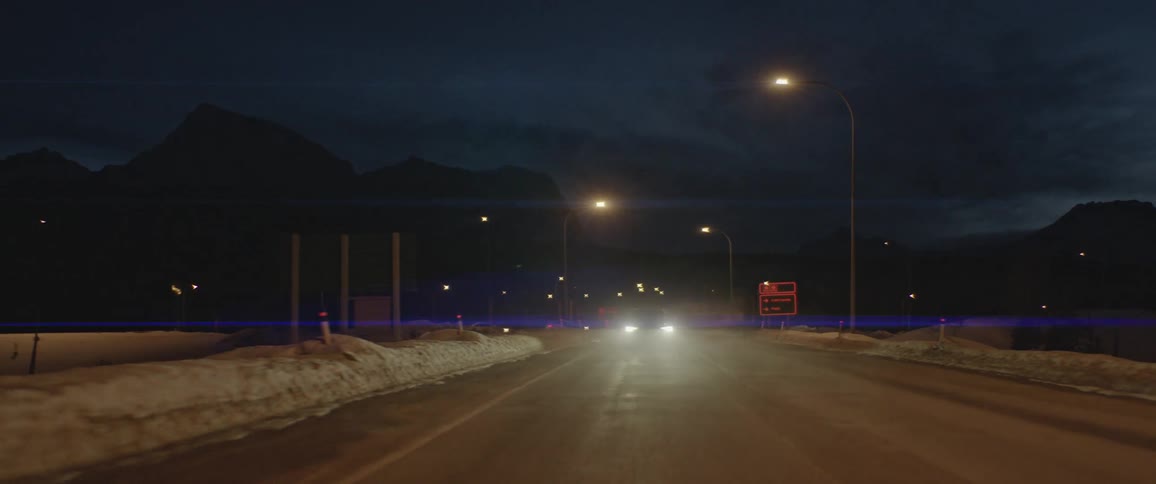 A vehicle travels a snow dusted road at night
