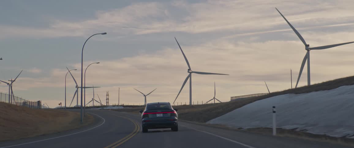 A vehicle driving on a road with wind turbines the sky and clouds in the background