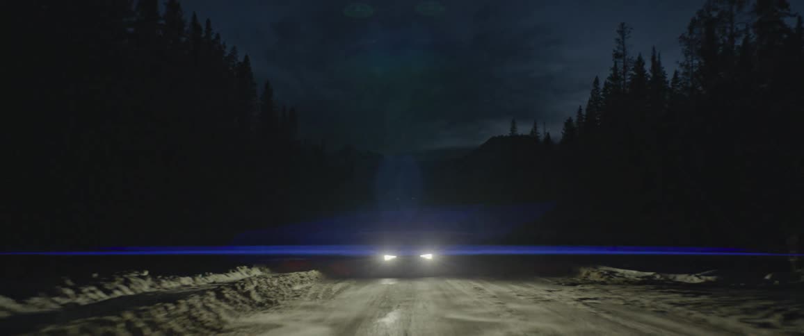 Dark grey audi illuminate the snowy forest road at night