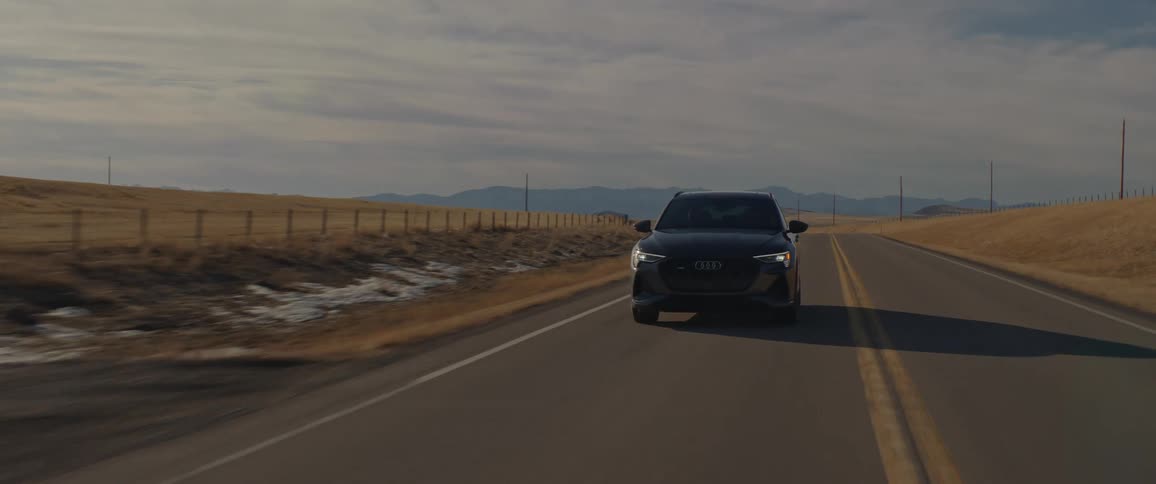 Dark grey audi car travels along highway in the field