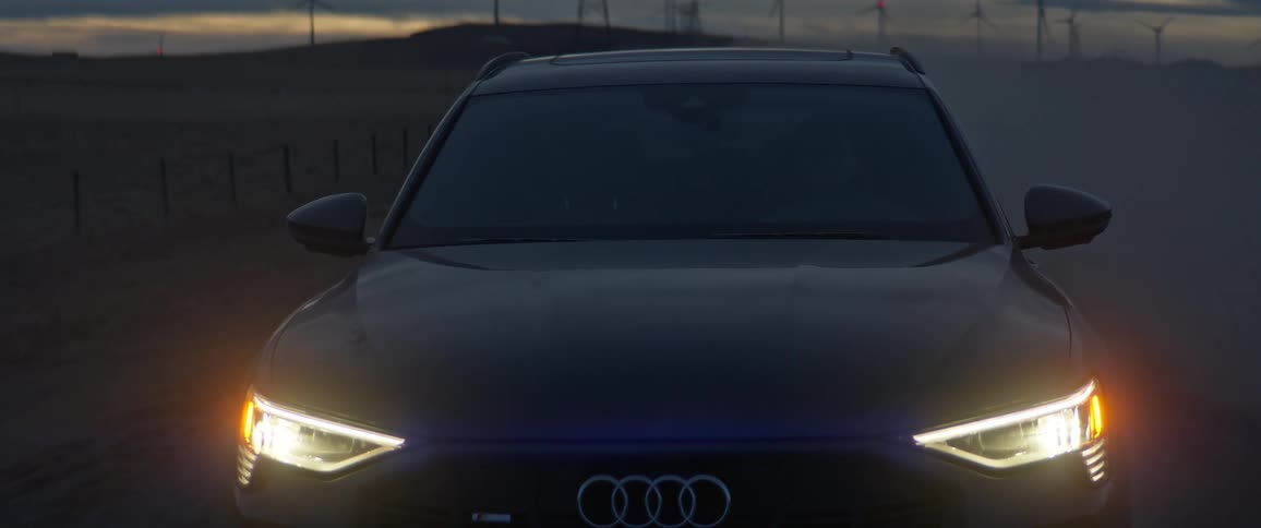 Black sports car with headlights on driving on a rural road next to transmission towers at evening