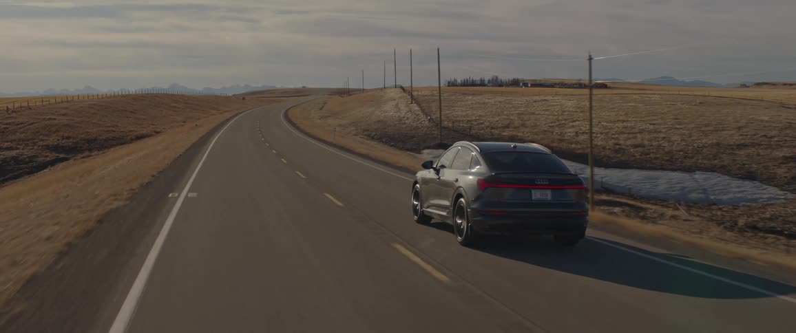 A vehicle driving on a road with the landscape the sky and clouds in the background