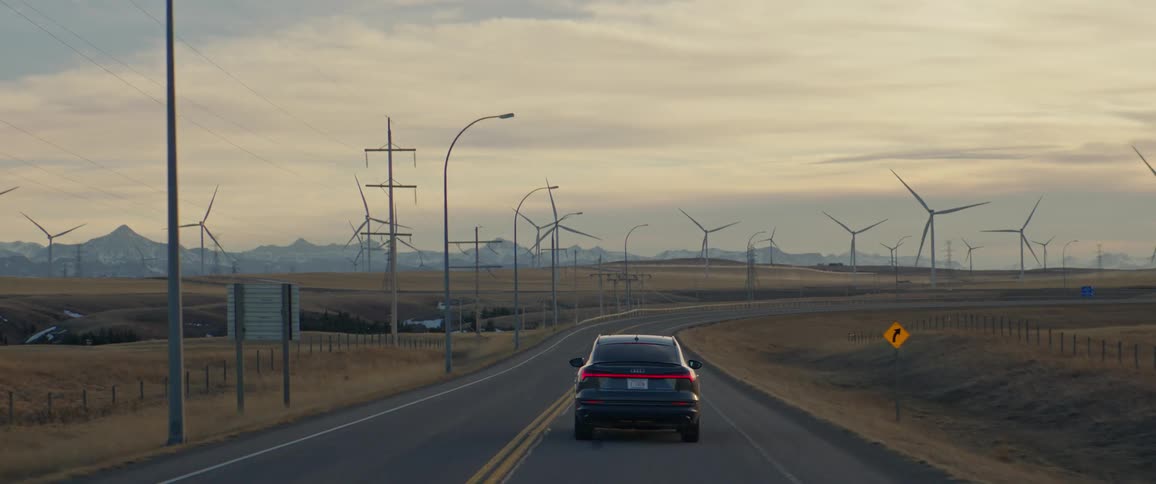 A black car travels on a road through a wind farm of spinning turbines