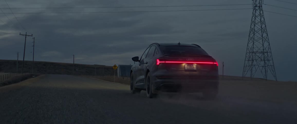 Dark grey audi car travels on dirt road with utility poles in the background