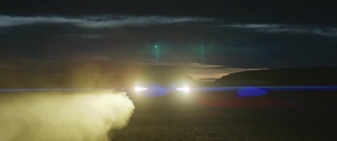 A vehicle with headlights driving on a road with smoke with the sky and clouds in the background